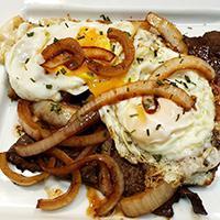 Sirloin Steak & Eggs (Bistec al Caballo) · A mouth-watering sirloin steak and onions topped with two fried eggs.