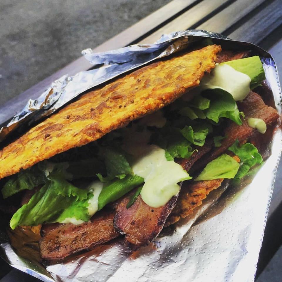 BLT Patacon · Smashed plantain sandwich stuffed with double smoked bacon, green leaf lettuce, tomatoes, and salsa verde.