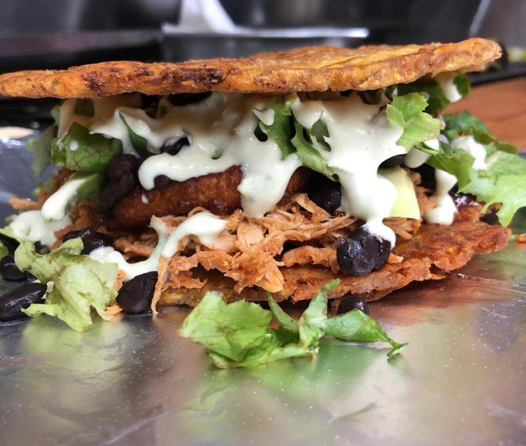 Pulled Roasted Pork Patacon · Smashed green plantain sandwich stuffed with pulled roasted pork, fried queso blanco, green leaf lettuce, tomatoes, ketchup, and salsa verde. 