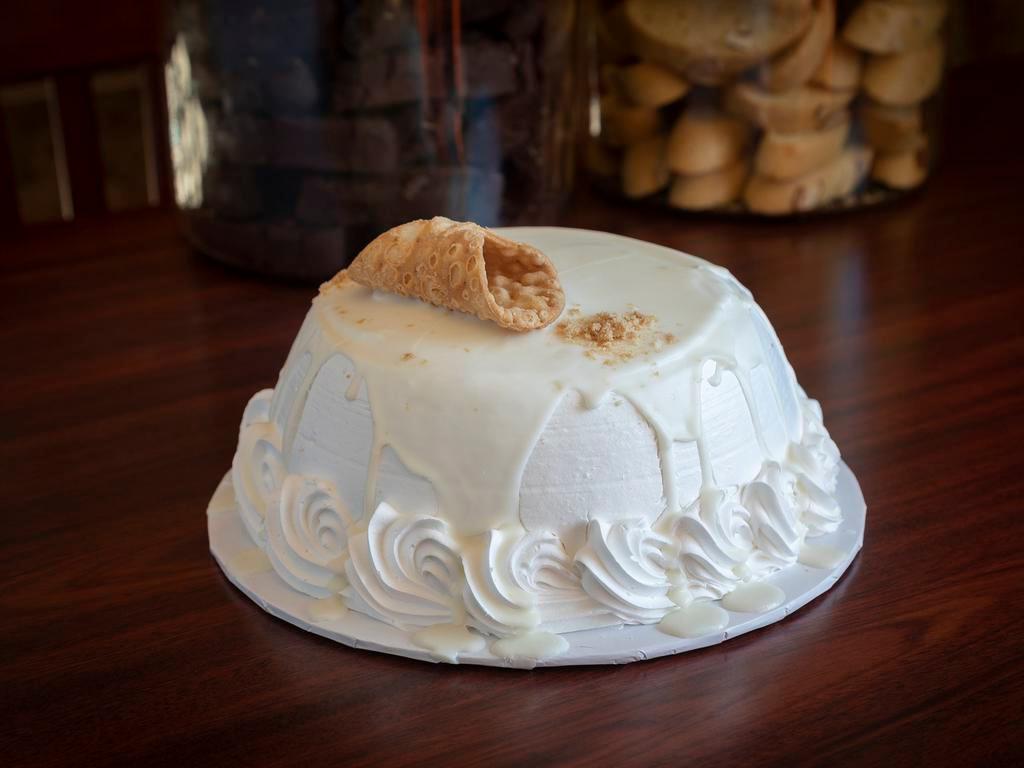 White Cannoli Cake · White cake filled with our famous cannoli filling covered in white Italian cream and white chocolate ganache with a cannoli on top.