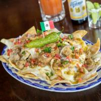 Nachos Chingones · Homemade corn tortilla chips layered with tender pork green chile, melted Oaxaca cheese, roa...