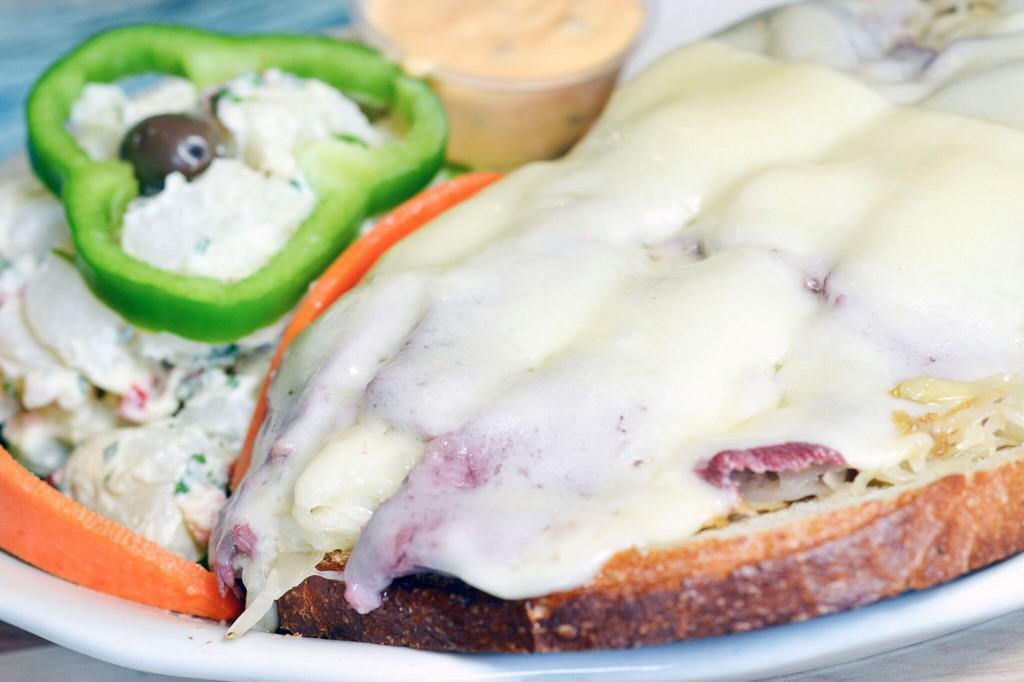 Reuben Sandwich · Grilled corned beef and tangy sauerkraut on rye bread topped with melted Swiss cheese and served with potato salad and  pickle.