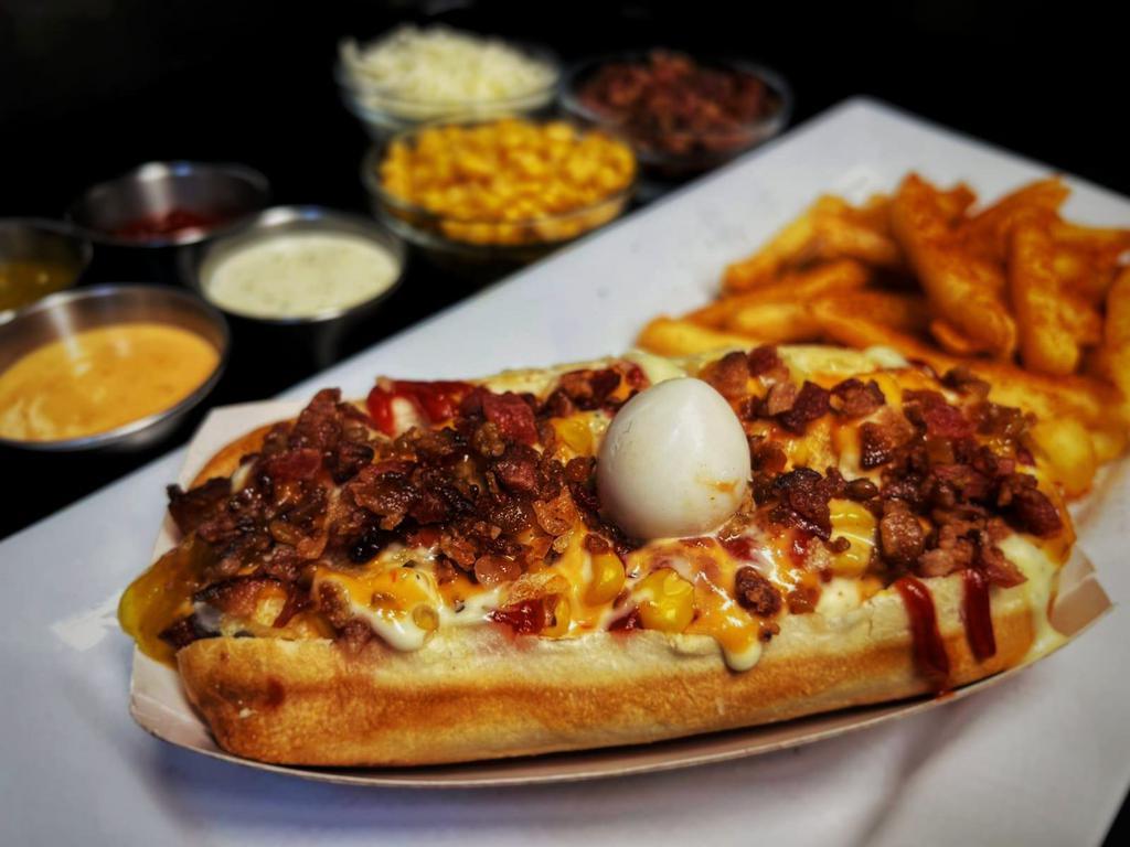 Chori-perro · Hot dog Bun, grilled Colombian Chorizo, mozzarella, sweet corn, crushed potato chips, onions, pineapple sauce, pink sauce, garlic mayo, ketchup, bacon bits  topped with a boiled quail egg and served with fries