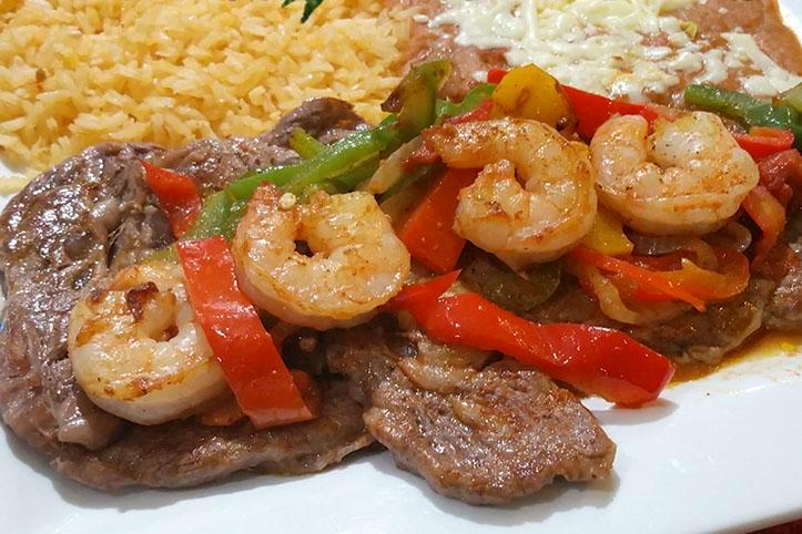 Steak and Shrimp · Rib-eye steak, grilled shrimp, bell peppers, tomatoes, and onions on top. Served with rice, beans refried or black, lettuce, guacamole, pico de gallo, and tortillas flour or corn.