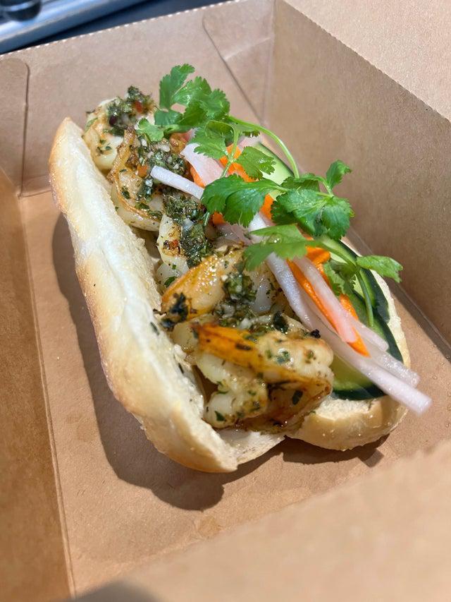 Spiced Chimi Shrimp Banh Mi Sandwich · Shrimp marinated in spiced chimi. Served on a toasted hero roll and mayo spread. Garnished with sliced cucumbers, pickled veggies, and fresh cilantro. Side of jalapeno.