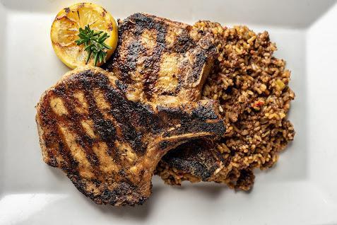Grilled Pork Chops · Two grilled pork chops served over a bed dirty rice with collard greens