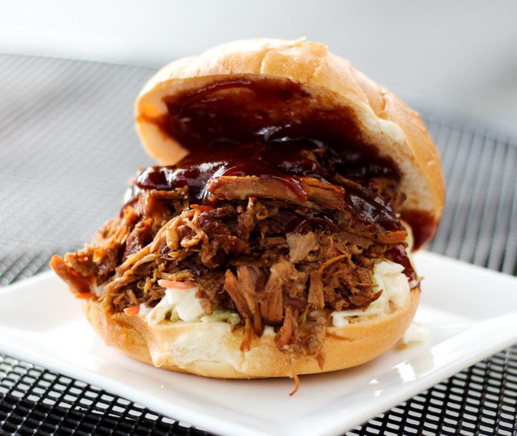 Root Beer Pulled Pork Sandwich · Tender pork shoulder slowly braised in root beer and herbs and spices. On a fresh bakery bun, BBQ sauce and house slaw.