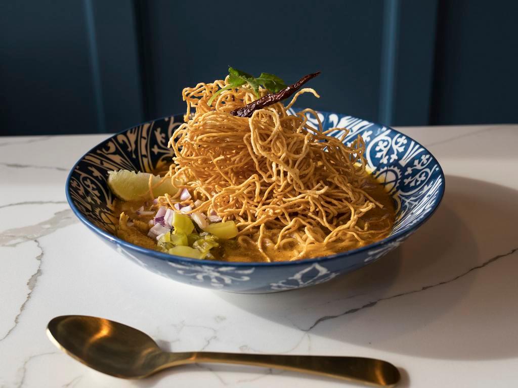 Kao Soi · Egg noodles and chicken thigh or vegetables simmered in curry soup, topped with crispy egg noodles, served with pickled mustard green, red onion, lime and chili oil.