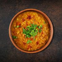 Lentil Legacy · Yellow dal cooked in a pot with chilies, onion, spices and herbs. Served with side of rice.
