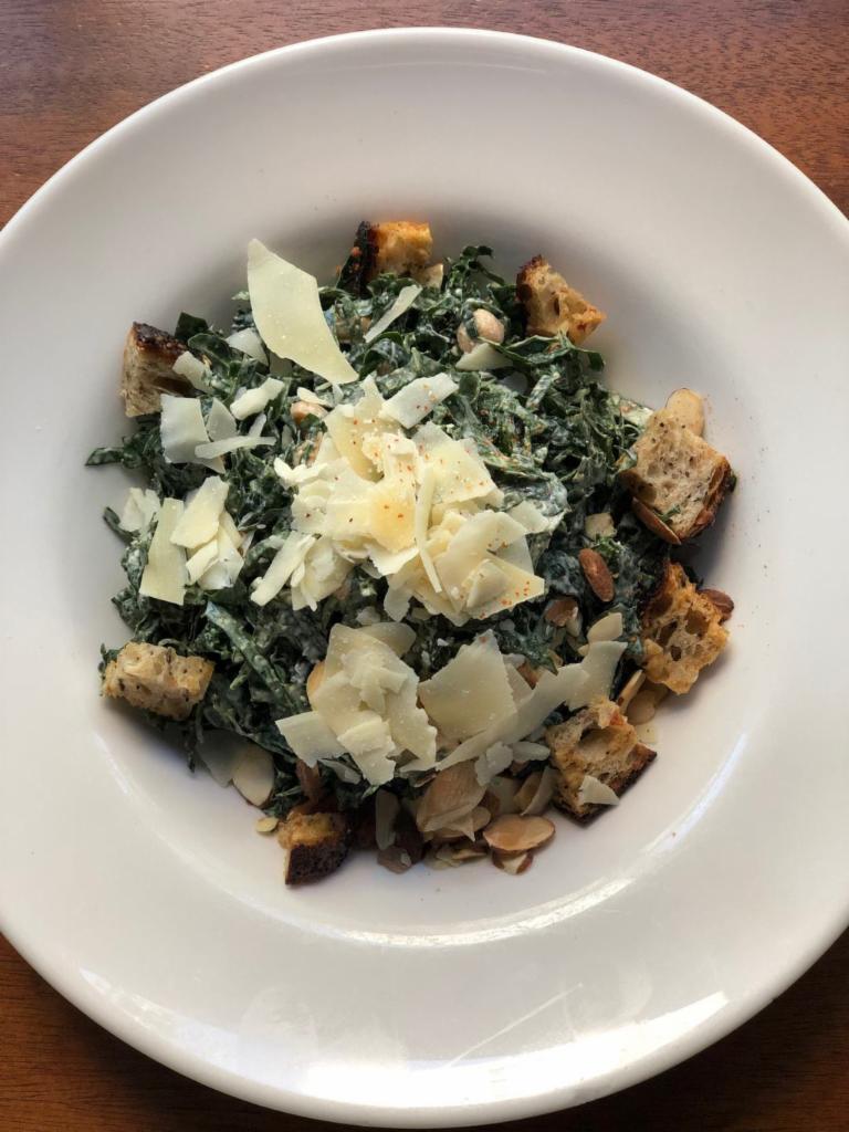 Spicy Kale Caesar Salad · Chopped kale, slivered almonds, chickpeas, parmesan, seeded sourdough croutons and spicy caesar dressing.