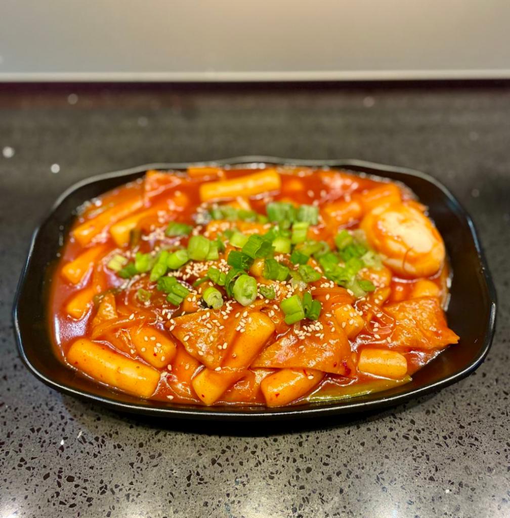 Spicy Stir-Fried Rice  (Tteokbokki - 떡볶이) · Classic Korean Dish. Korean Rice Cake (떡) cooked in a spicy sauce along with Korean Fish Cake (오뎅), white onion, and green onion. Topped with a hard boiled egg, chopped scallion and toasted sesame seeds.