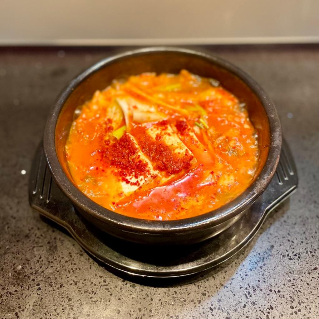 Kimchi Stew (Kimchi-Jjigae - 김치찌개) · A stew utilizing our very own kimchi made by K-Top's owner herself. The kimchi is pan-simmered before being placed in a stone bowl, along with scallion, white onion, tofu, and sliced pork belly. It is then set to stew on top of a fire until it reaches a delicious boiling consistency. Served with a serving of rice.
