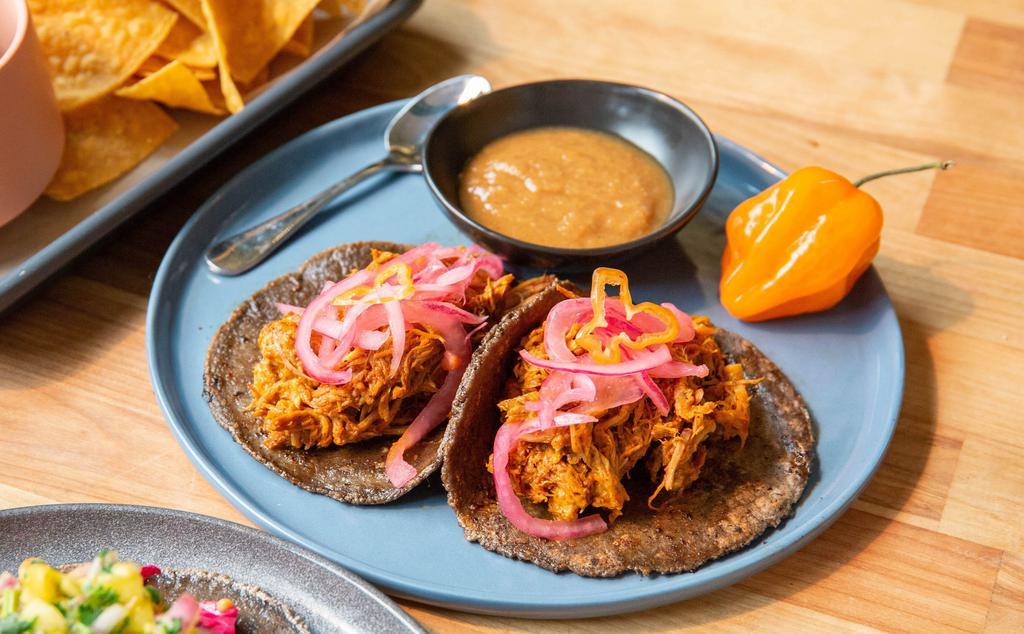 2 Cochinita Tacos · Slow-roasted pork in achiote and banana leaf, served on 3 sisters corn tortilla with habanero pickled red onions.