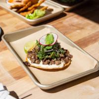 Tostada Ahumada · Tostada topped with smoked skirt steak, melted oaxaca cheese, caper aioli, microgreens, and ...