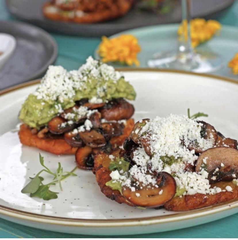 Los Maduros Vegetariano · Two fried ripe plantains topped with sauteed mushrooms, grilled scallions, recado negro, guacamole, and cotija cheese. Drizzled with chimichurri on top.
