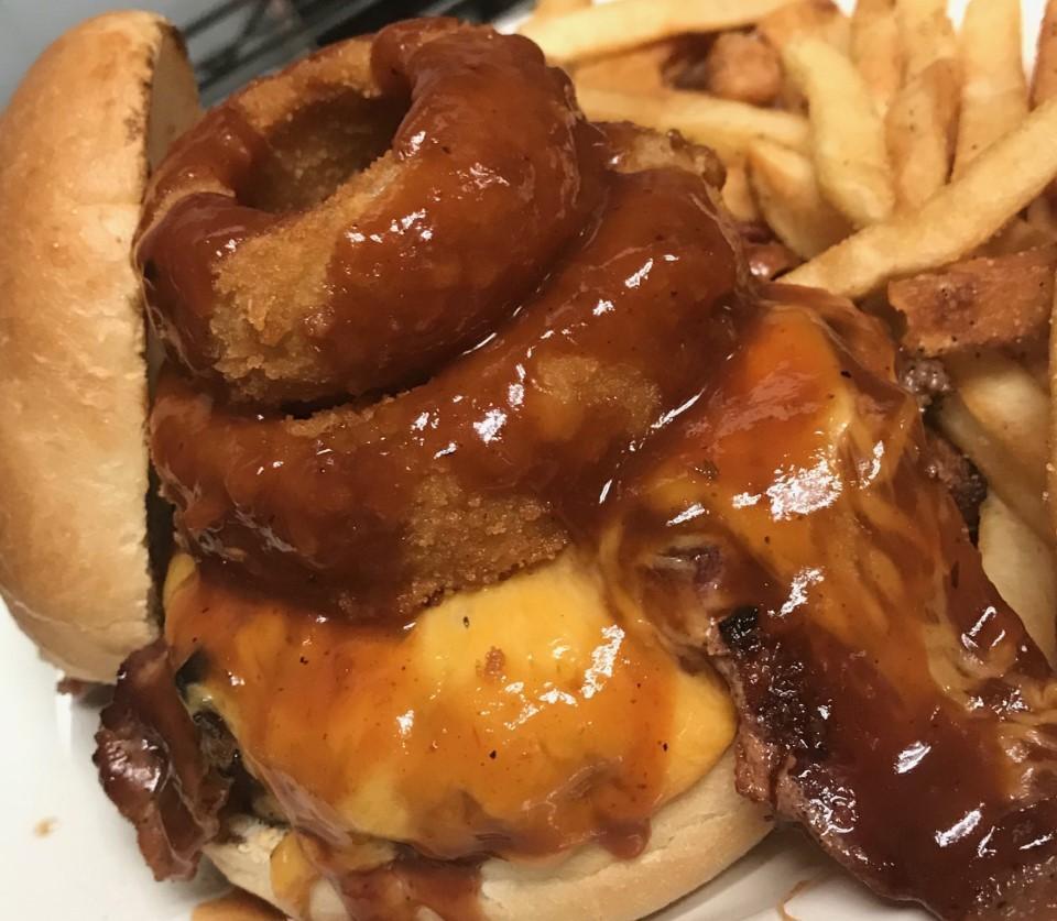 BBQ Hog Burger · 1/2 lb. burger, bacon, bbq pulled pork, cheddar cheese and topped with an onion ring. Dressed with lettuce, tomato and served with fries.