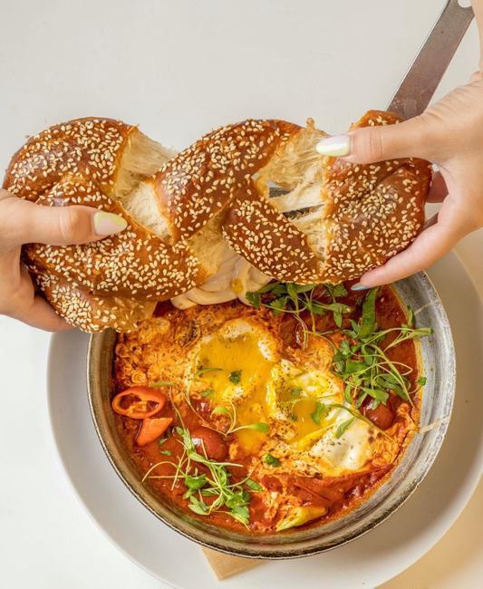 Shakshuka · poached eggs in a fresh tomato sauce, zaatar, tahini, cilantro, and served with freshly baked challah bread