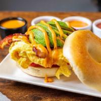 Bacon Avo Tom Bagel · Eggs, bacon, avocado and tomato and chipotle drizzle on a toasted plain bagel.