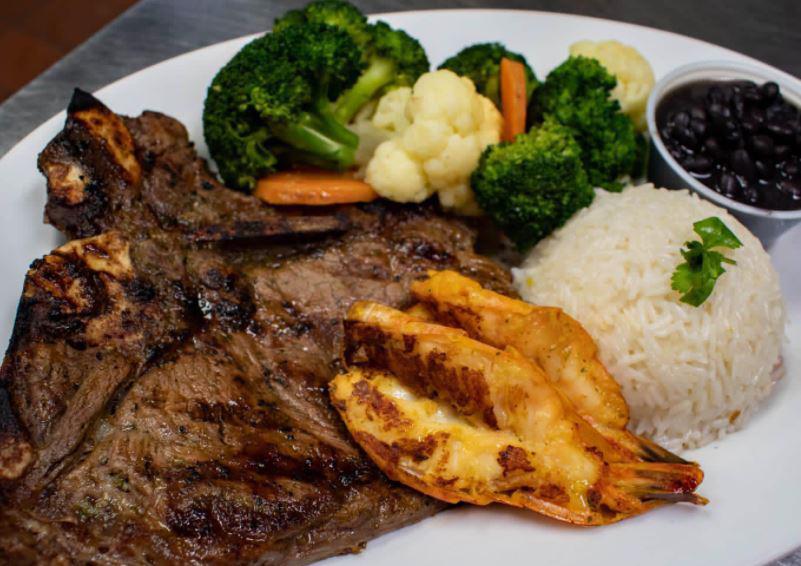 Grilled T-Bone Steak · T-bone steak, grilled jumbo shrimp, served with rice, and beans.