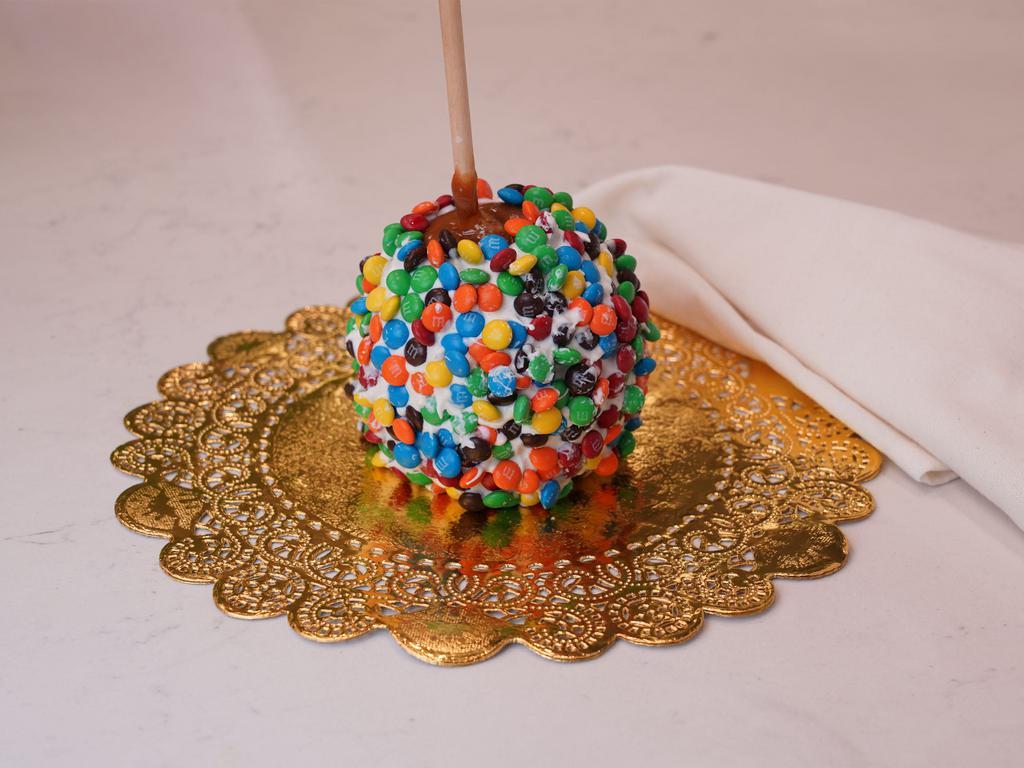 Rainbow M&M Caramel Apple · Caramel apple dunked in white chocolate then rolled in colorful M&Ms and finished with a white chocolate drizzle.