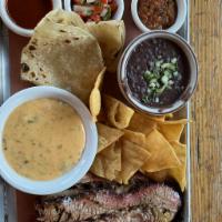 Plato Tejano (Brisket) · Sliced smoked brisket with refried black beans, tortillas, chips, salsa, and queso 