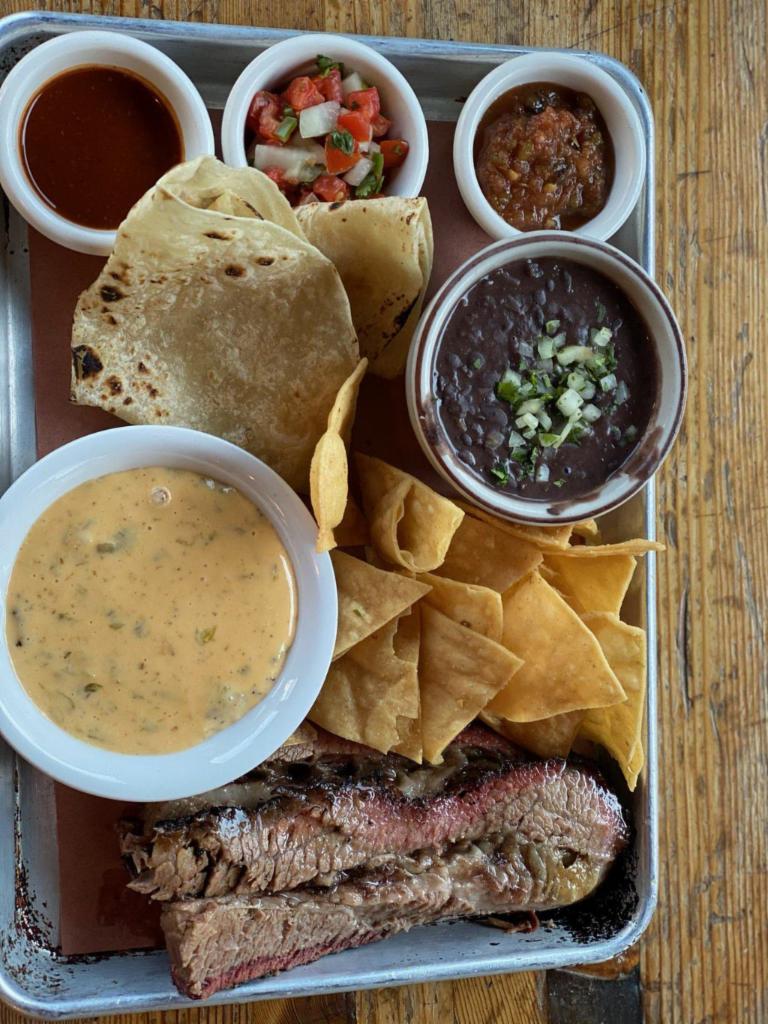 Plato Tejano (Brisket) · Sliced smoked brisket with refried black beans, tortillas, chips, salsa, and queso 