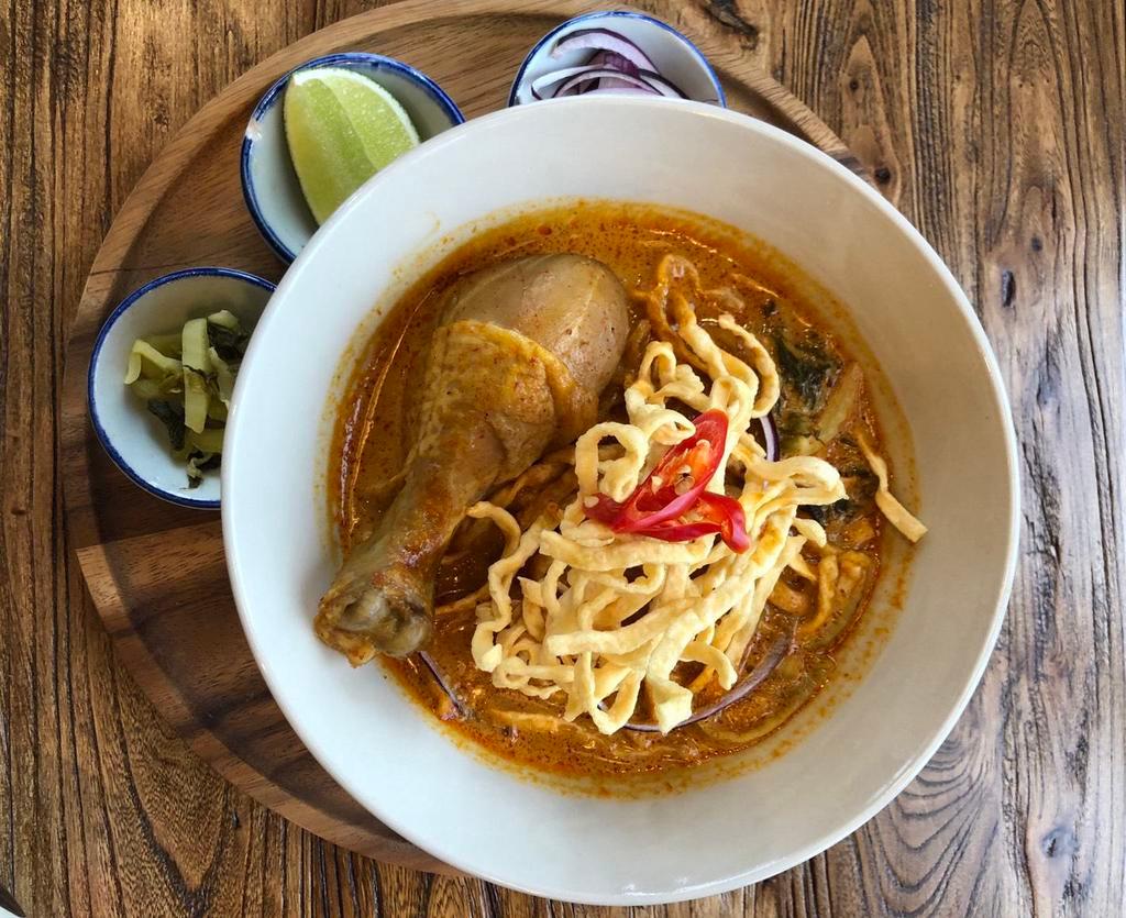 Chiang Mai Curry Noodle Soup · Northern Thai style noodles with slow braised chicken leg on the bone topped with pickled mustard greens, red onion, fried shallots and crispy egg noodles in turmeric coconut curry sauce.