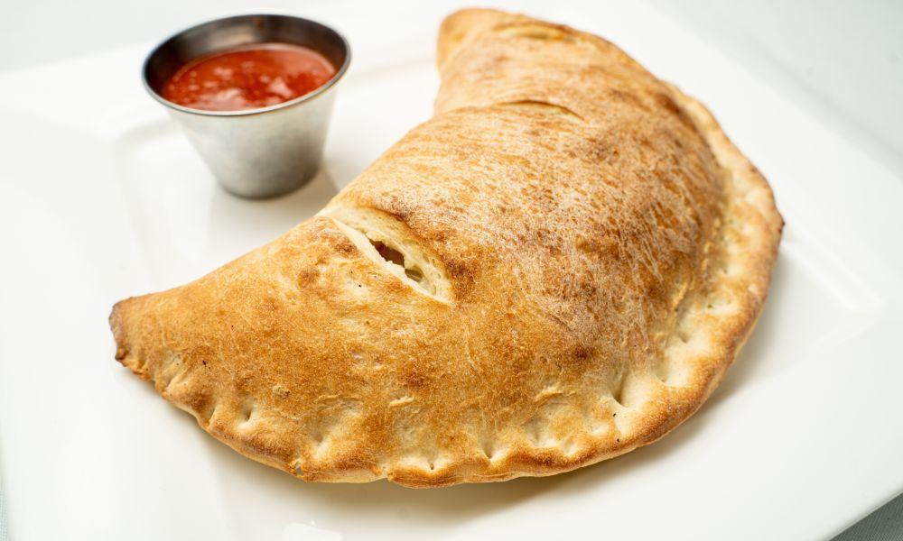 Veggie Calzone · Fresh Dough stuffed with Mushrooms, Green Peppers, Tomatoes, Onions, Spinach, and mozzarella cheese. Served with a side of homemade Marinara.