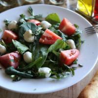 Spinach Caprese Salad · Slices of tomato on a bed of spinach, fresh mozzarella balls, basil, and drizzled with olive...