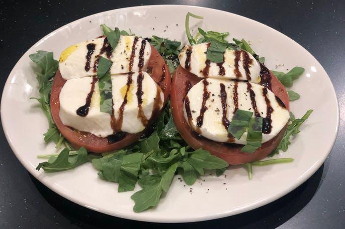 Caprese Salad · Fresh mozzarella, heirloom tomatoes and basil on a bed of arugula with a balsamic drizzle.