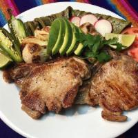 Chuletas Asadas con Nopales y Cebollitas · Grilled pork chops with cactus and scallions served with rice and beans, and tortillas or br...