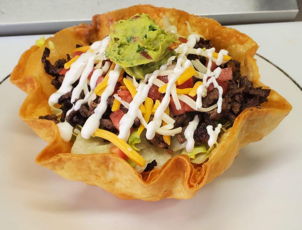 Taco salad · Large round shell filled with beans, rice, lettuce, diced tomatoes, shredded cheese, sour cream, guacamole, and your choice of meat.