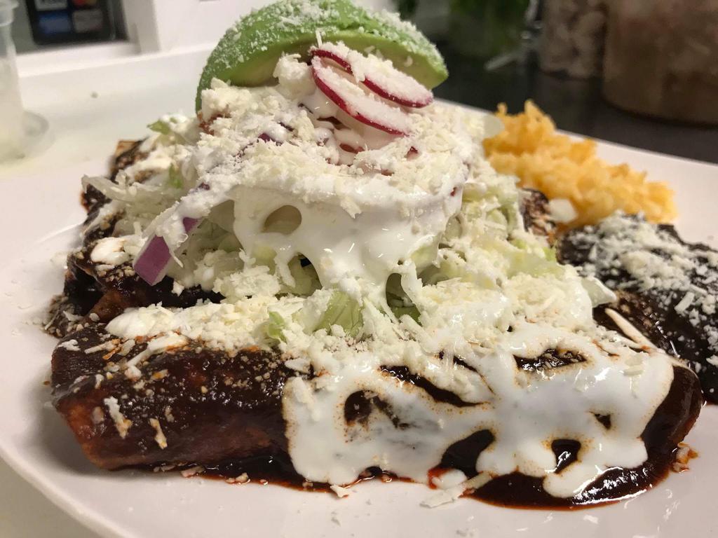 Enchiladas De Mole · 3 fresh home made gluten free corn tortillas in Red mole, chocolate, chile, lettuce, sour cream, cheese, onion and avocado with a side of beans and rice.
