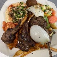 Lamb Chops · Marinated in a special seasoning served on a plate with a side salad, hummus, pita bread and...