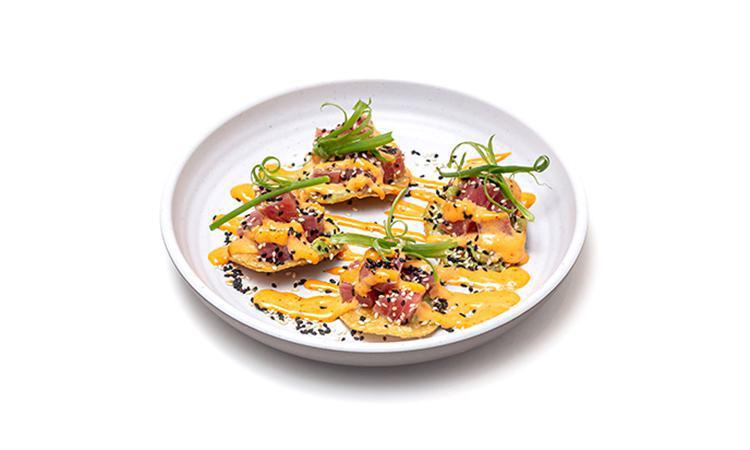 Spicy Tuna Tostada · Fresh, raw sushi-grade ahi tuna tossed with sesame, scallions and lightly dressed with a spicy Sriracha sauce. Served on top of yellow corn tostadas with avocado, smoked paprika and micro-cilantro.