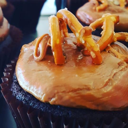 Caramel Crunch Cupcake · Chocolate cupcake topped with our signature caramel buttercream and garnished with pretzels, caramel         sauce, and a touch of sea salt!