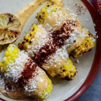 GRILLED CORN · Three half ears of corn on the cob grilled and topped with a garlic-lime aioli and cotija ch...