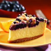 Lemon Blueberry Crumb Cheesecake（Slice） · A creamy lemon cheesecake topped with blueberries and brown sugar crumbs, sits on a cookie b...