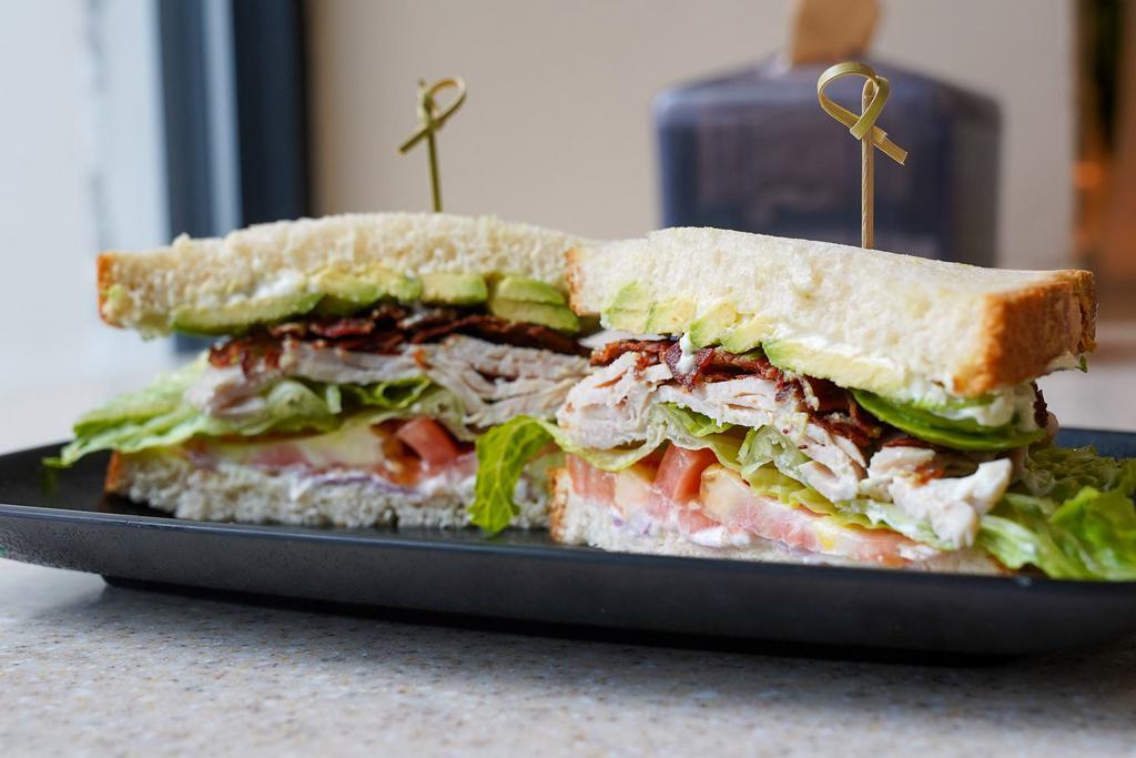 Turkey Avocado Club · Turkey, Mayo, Romaine Lettuce, Tomato, Bacon, Red Onion, Avocado on White Bread. Comes with Chips and a Pickle.