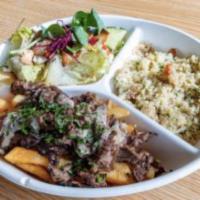 Steak Shawarma Plate · Steak topped with tahini sauce on bed of fries. pretty salad and couscous.
