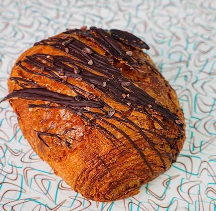 Chocolate Croissant · A flakey chocolate croissant filled with 64% dark chocolate sticks and topped with cacao nibs.