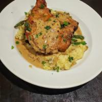 PAN FRIED PORK CHOP · A Thick cut pork chop on a bed of Mashed potatoes topped with sautéed green beans and our mu...