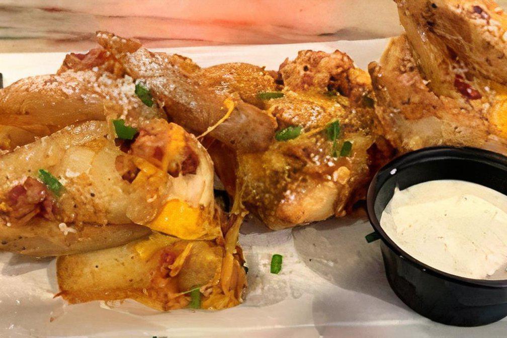 CHEDDAR BACON WEDGES · Smothered in cheddar cheese and hickory smoked bacon bits topped with fresh chives and served with a side of ranch dressing