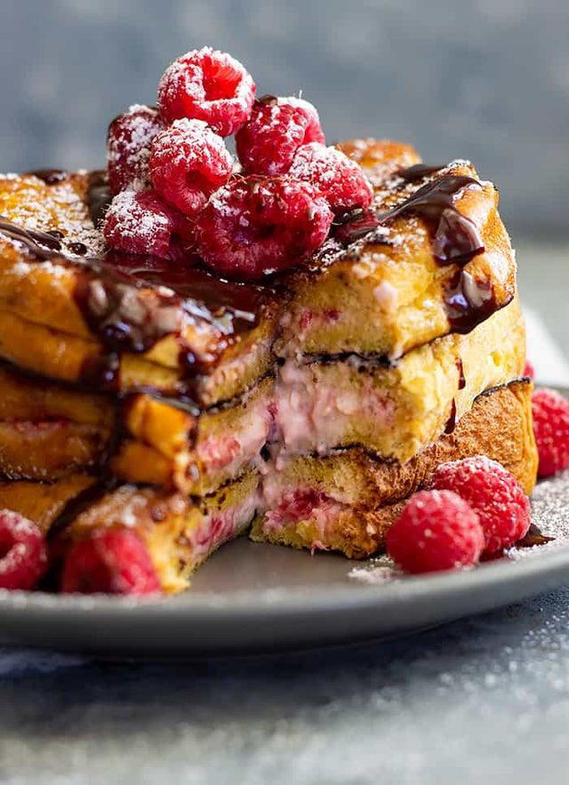 Cheesecake Brioche French Toast · 3 brioche French toast with a cheesecake topping, raspberries, chocolate drizzle and whipped cream. Contains the following eggs, gluten and milk.