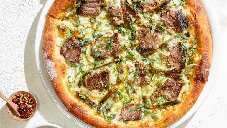 Carne Asada Pizza · Tender marinated steak, fire-roasted poblanos, cilantro pesto, yellow onions, Mozzarella, Monterey Jack and fresh cilantro. Served with housemade salsa verde.. [Calories listed are per slice. All pizzas are 6 slices.]