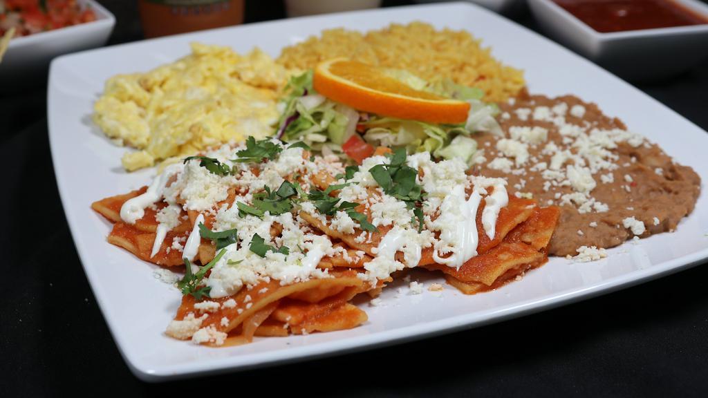 Chilaquiles Rojos · Red chilaquiles, tasty crunchy homemade tortilla chips, topped with our special tomato sauce, chopped onion, and cheese, served with two eggs, stewed potatoes, and fried beans topped with cheese.