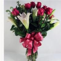 Debi Lilly Unforgettable Deluxe Arrangement · Roses, Lilies with greens in a clear garden vase with a bow. Roses can be red, pink, or yell...