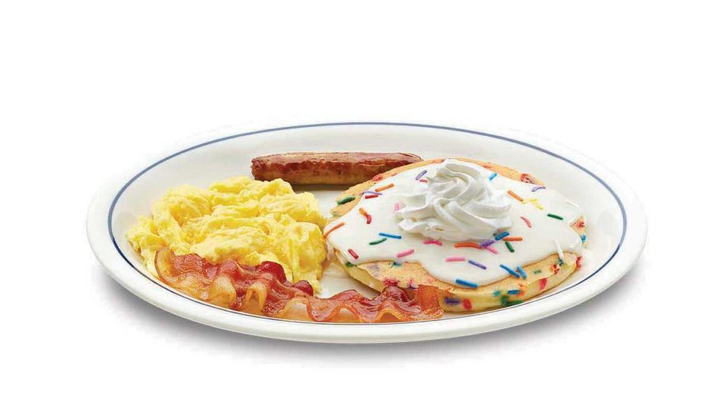 Cupcake Pancake Combo · One fluffy buttermilk pancake filled with festive rainbow sprinkles. Topped with cupcake icing & crowned with whipped topping. Served with 1 scrambled egg, 1 custom-cured hickory-smoked bacon strip & 1 pork sausage link.