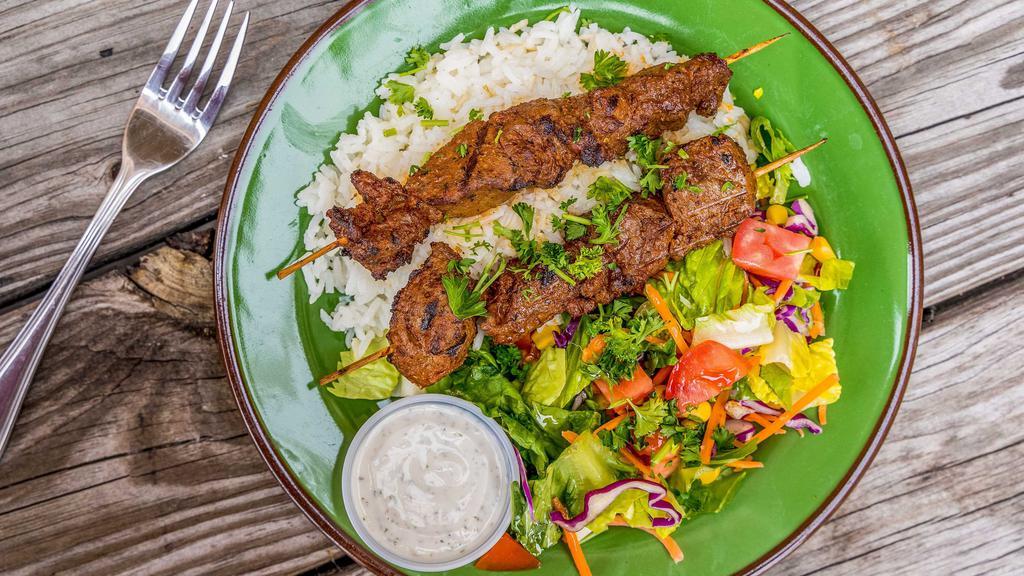 Lamb Shish Kebab · Grilled tender lamb chunks treated with house-made seasoning threaded on skewer. Served with salad, rice, and pita bread.