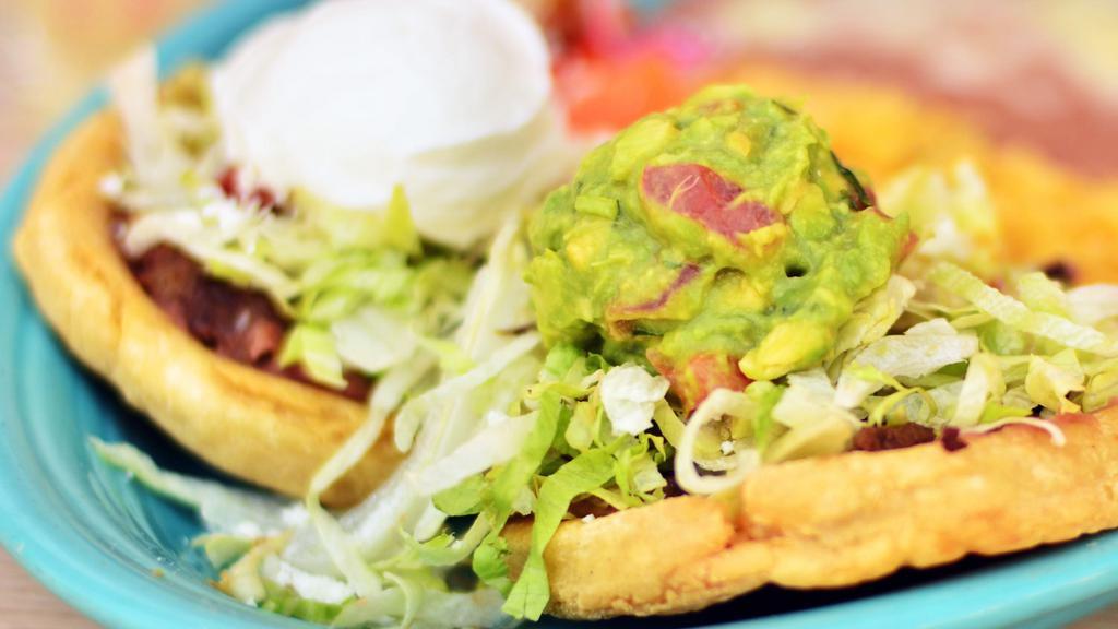Sopes Dinner Entree · Served with rice and beans. A thick round corn tortilla, fried and topped with refried beans, lettuce, sour cream, guacamole and your choice of meat. Garnished with cheese and taco sauce.